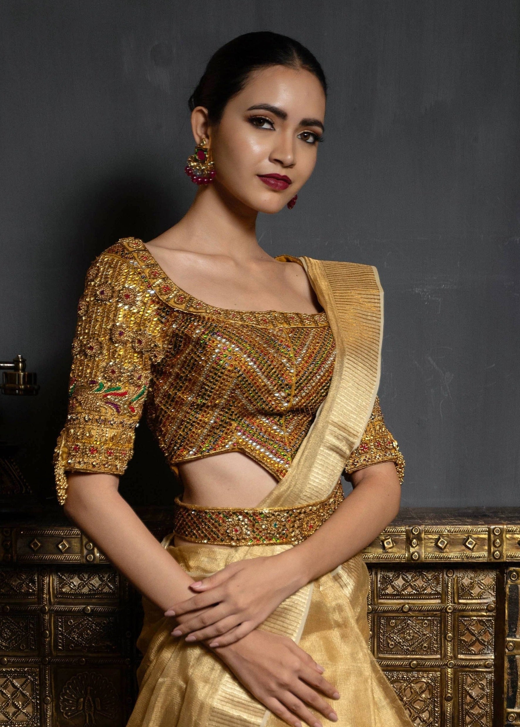 Model Preeti Kumari posing in a gold handcrafted raw silk blouse with heavy kemp embeliishment and goddess pendants on sleeves and matching belt. Looking at the camera.