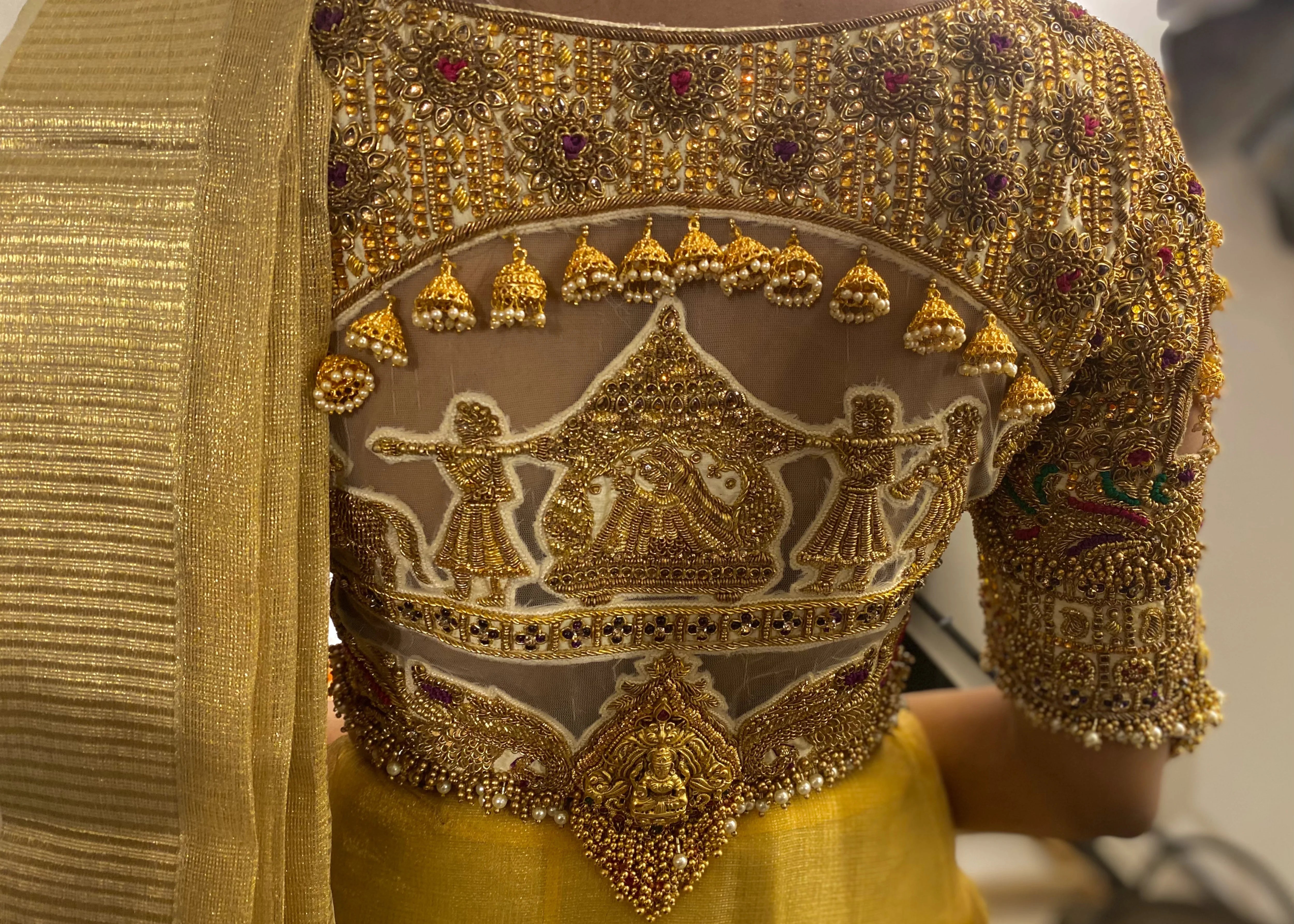 Model in a palanquin concept gold silk handcrafted blouse with heavy kemp and jhumki embeliishments and goddess pendants on sleeves.