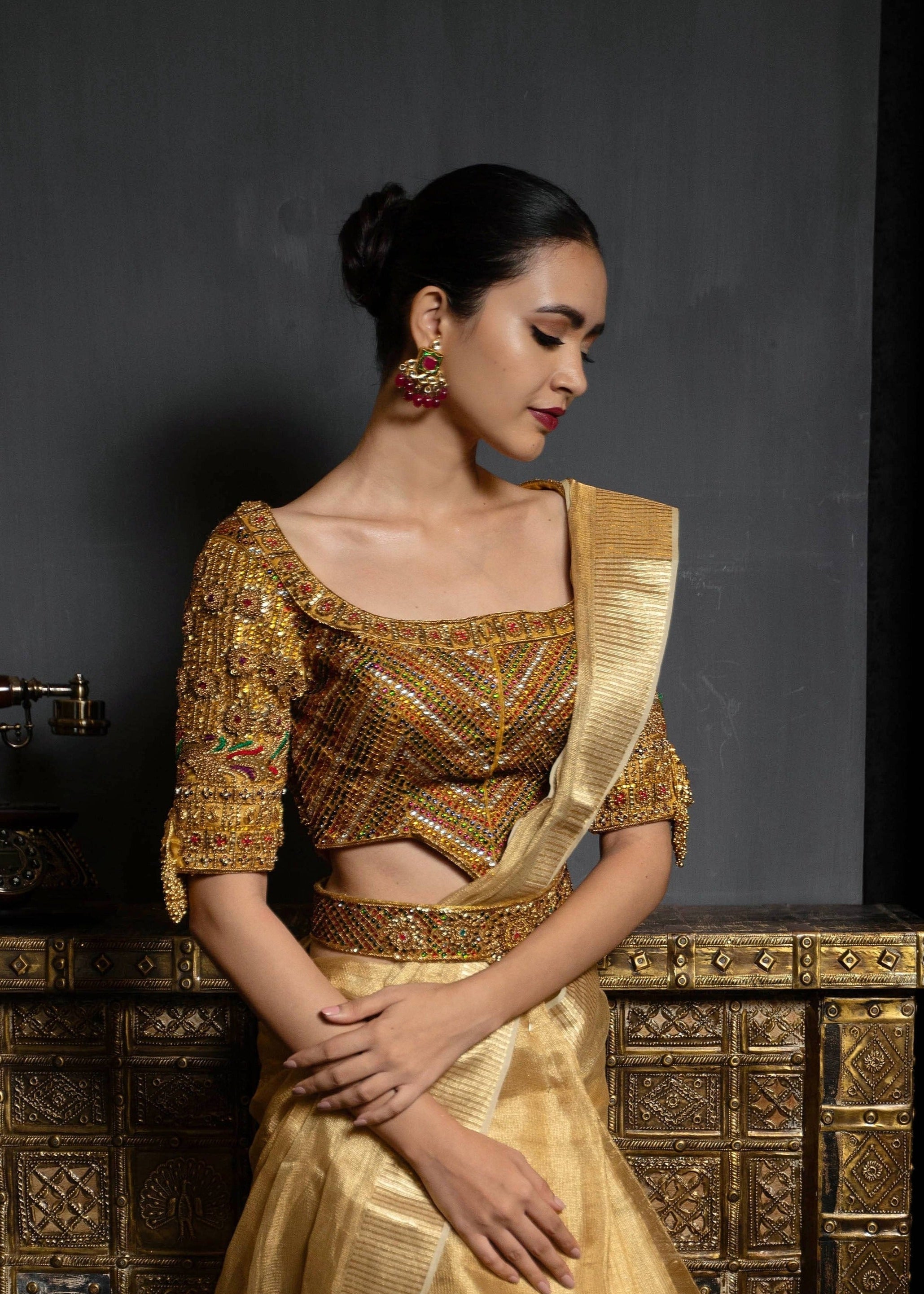Model posing in a gold handcrafted raw silk blouse with heavy kemp embeliishment and goddess pendants on sleeves and matching belt.