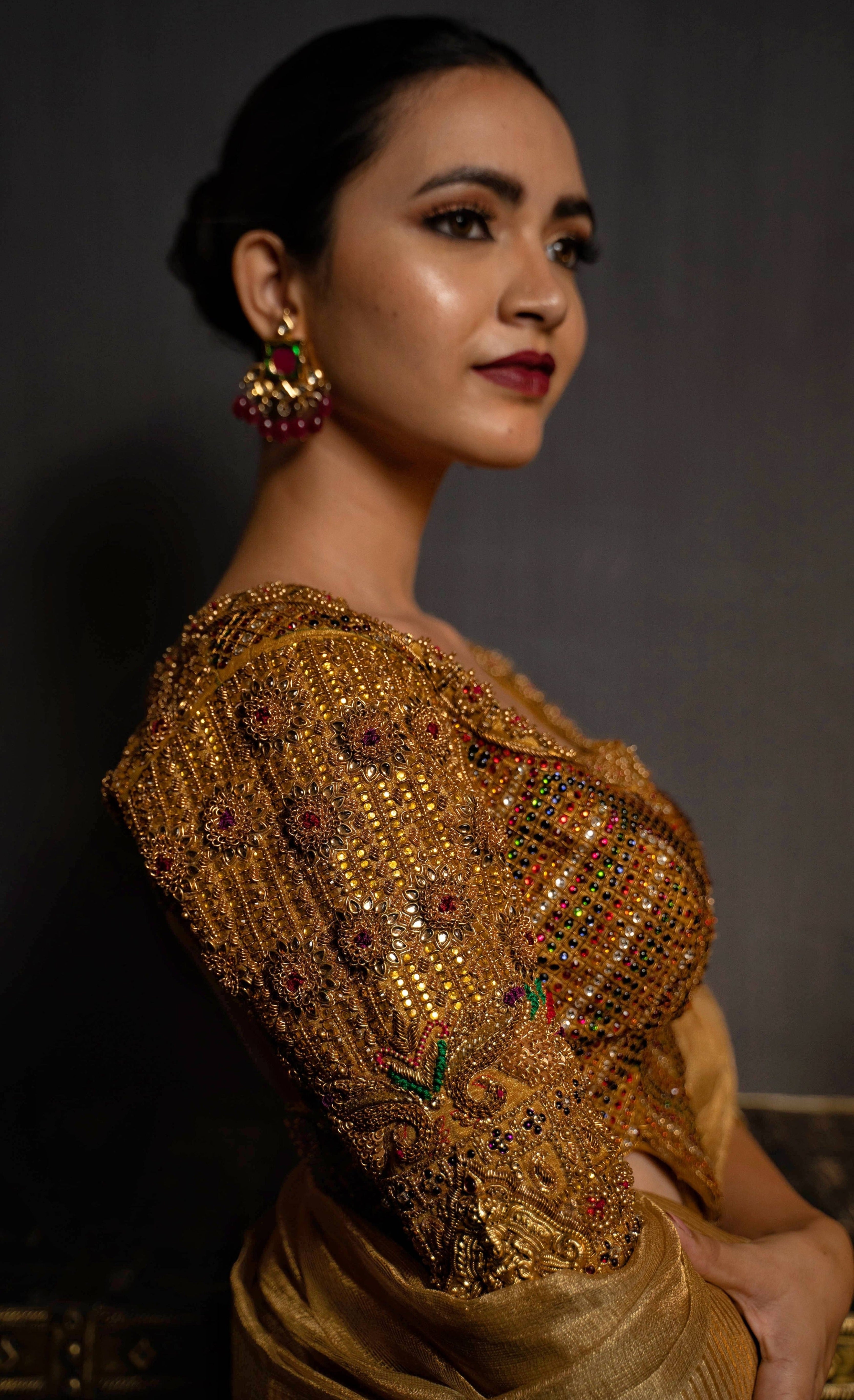 Model posing in a gold handcrafted raw silk blouse with heavy kemp embeliishment and goddess pendants on sleeves and matching belt. Blouse sleeves and work on cup.