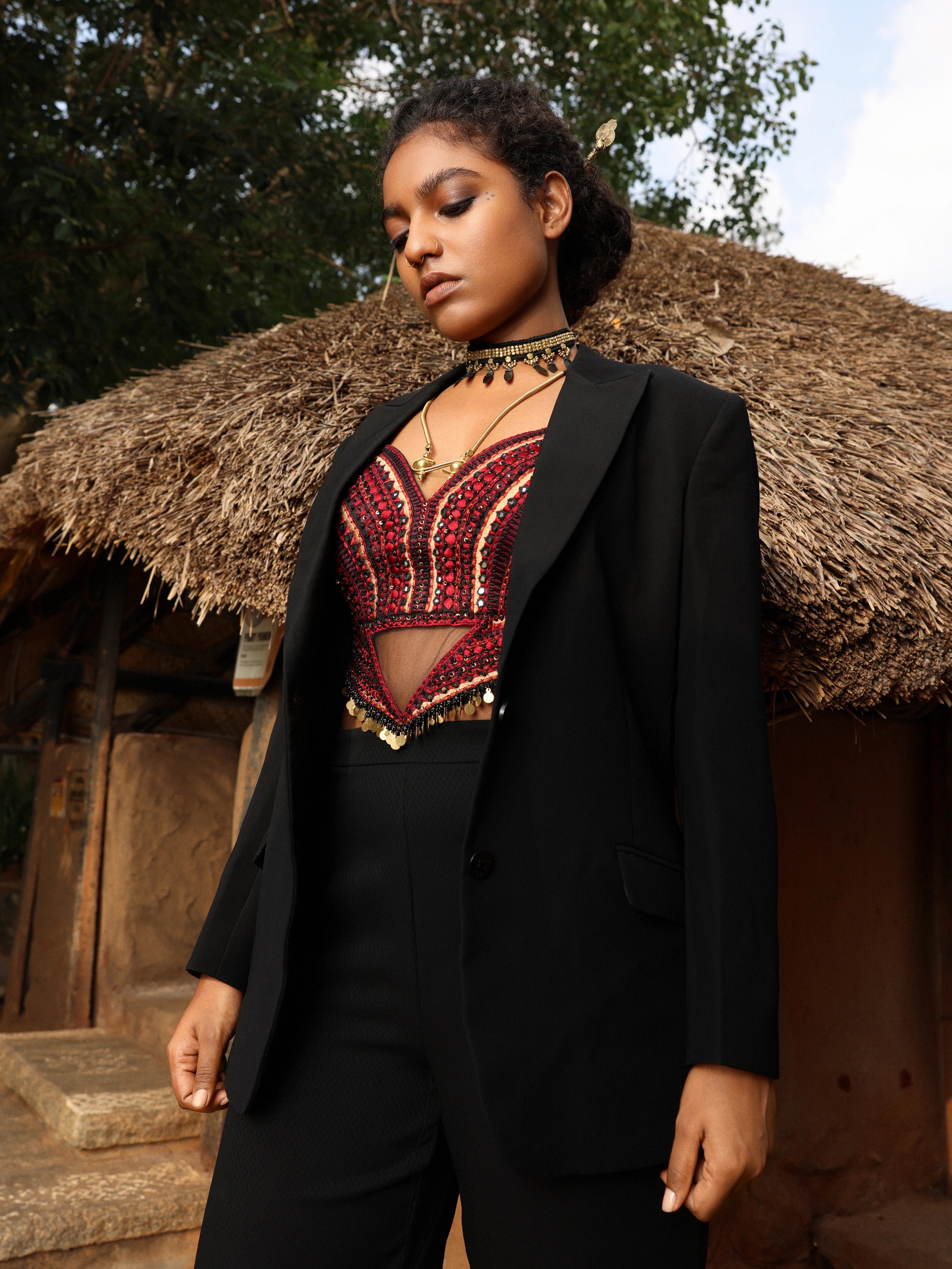 Model posing in black pantsuit with handcrafted corset. Posing outside a hut.