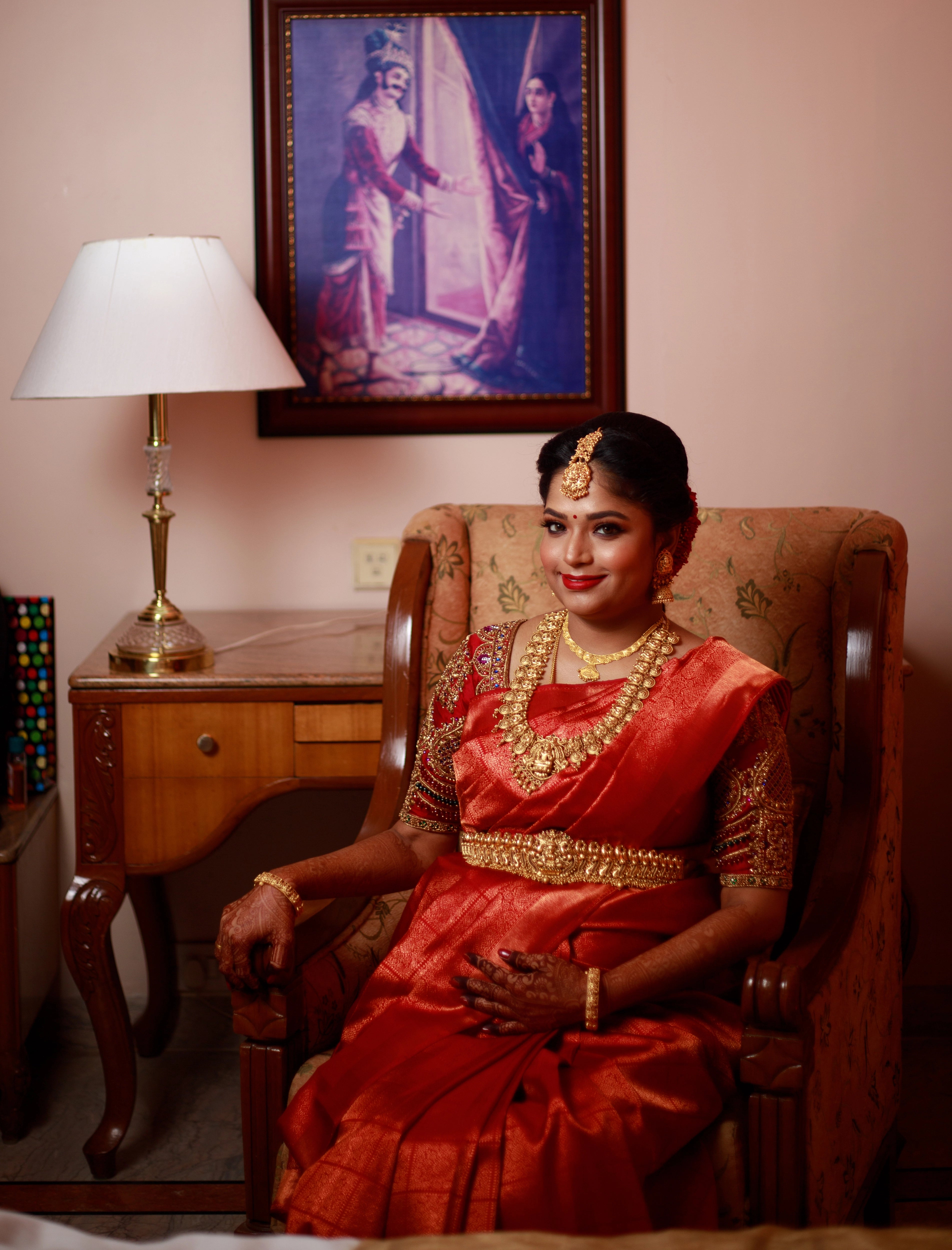 Mom to be Gayathri Kiran Kumar posing seated in a red silk blouse for her baby shower / seemantham, intricately handcrafted with kemp stones, zardozi and beads by team Archana Karthick.