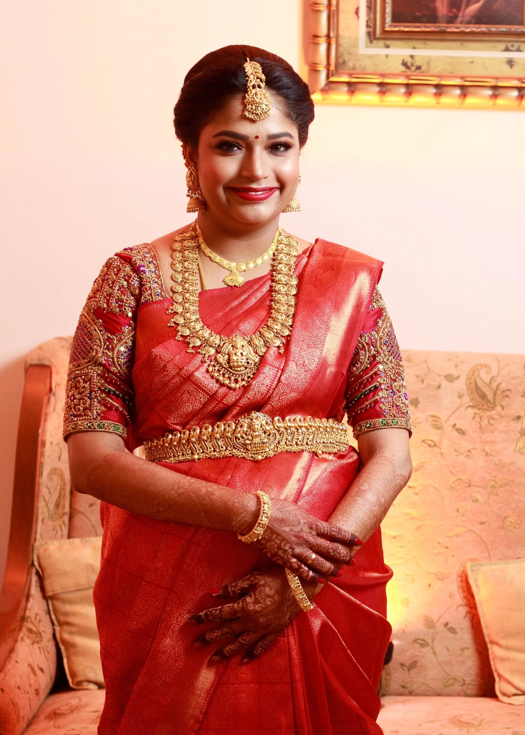 Mom to be Gayathri Kiran Kumar posing with a smile in a red silk blouse for her baby shower / seemantham, intricately handcrafted with kemp stones, zardozi and beads by team Archana Karthick.