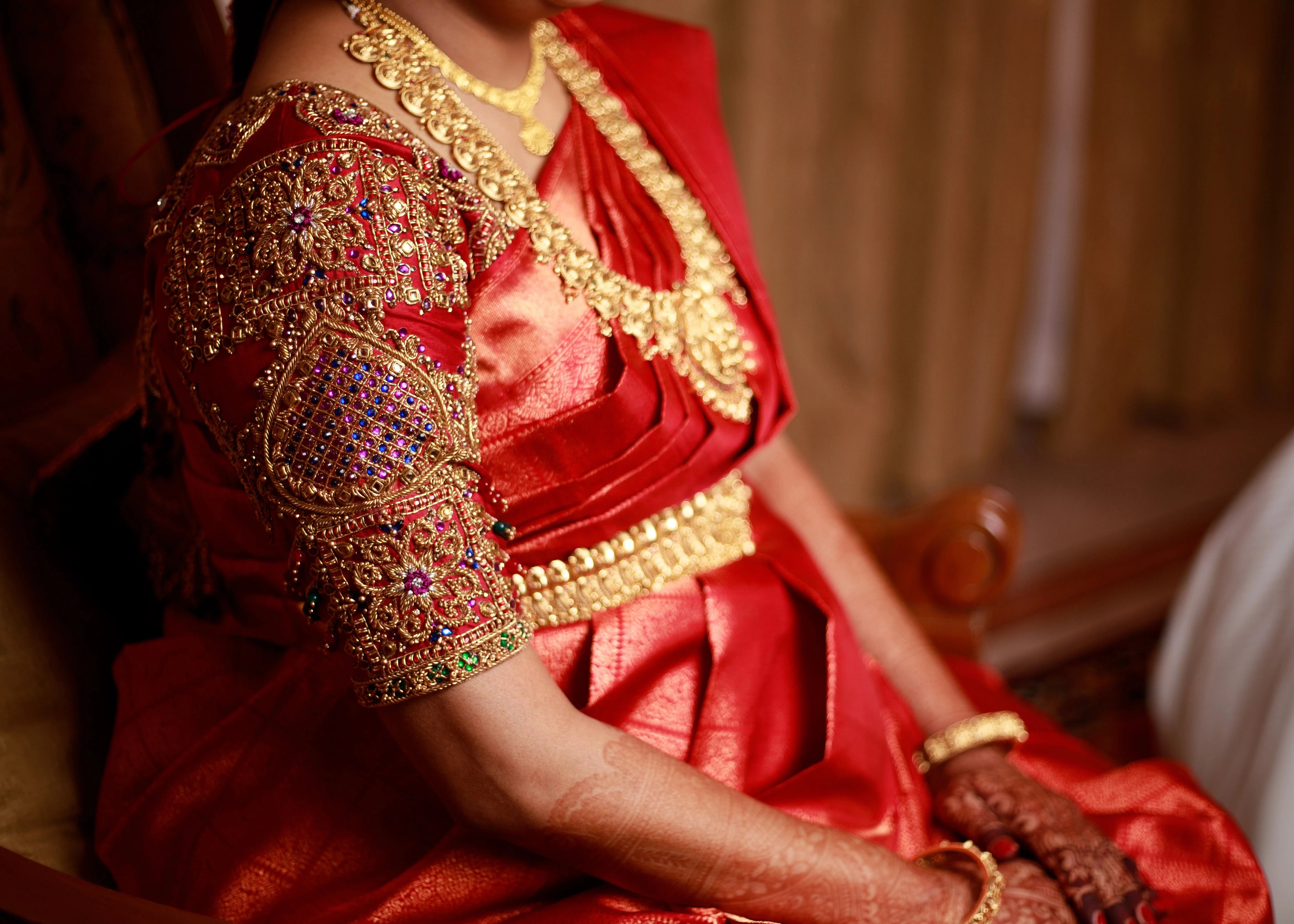 Mom to be Gayathri Kiran Kumar showcasing blouse sleeves in a red silk blouse for her baby shower / seemantham, intricately handcrafted with kemp stones, zardozi and beads by team Archana Karthick.