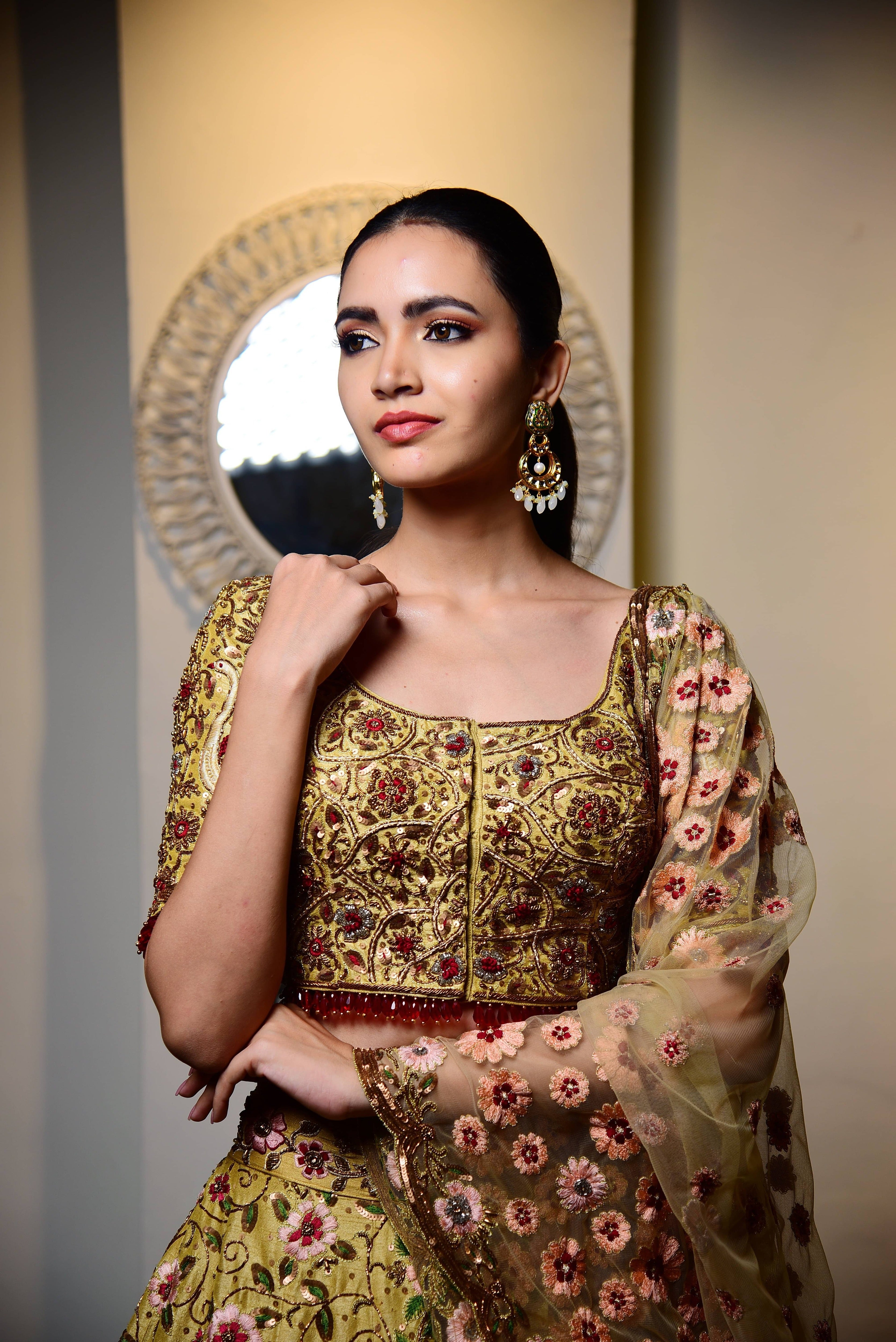 Model is seen here posing with a subtle smile. Raw silk lehenga with heavy intricate resham, sequins, beads,stonework embellishments all over the lehenga, blouse and tulle dupatta w front bouse view.