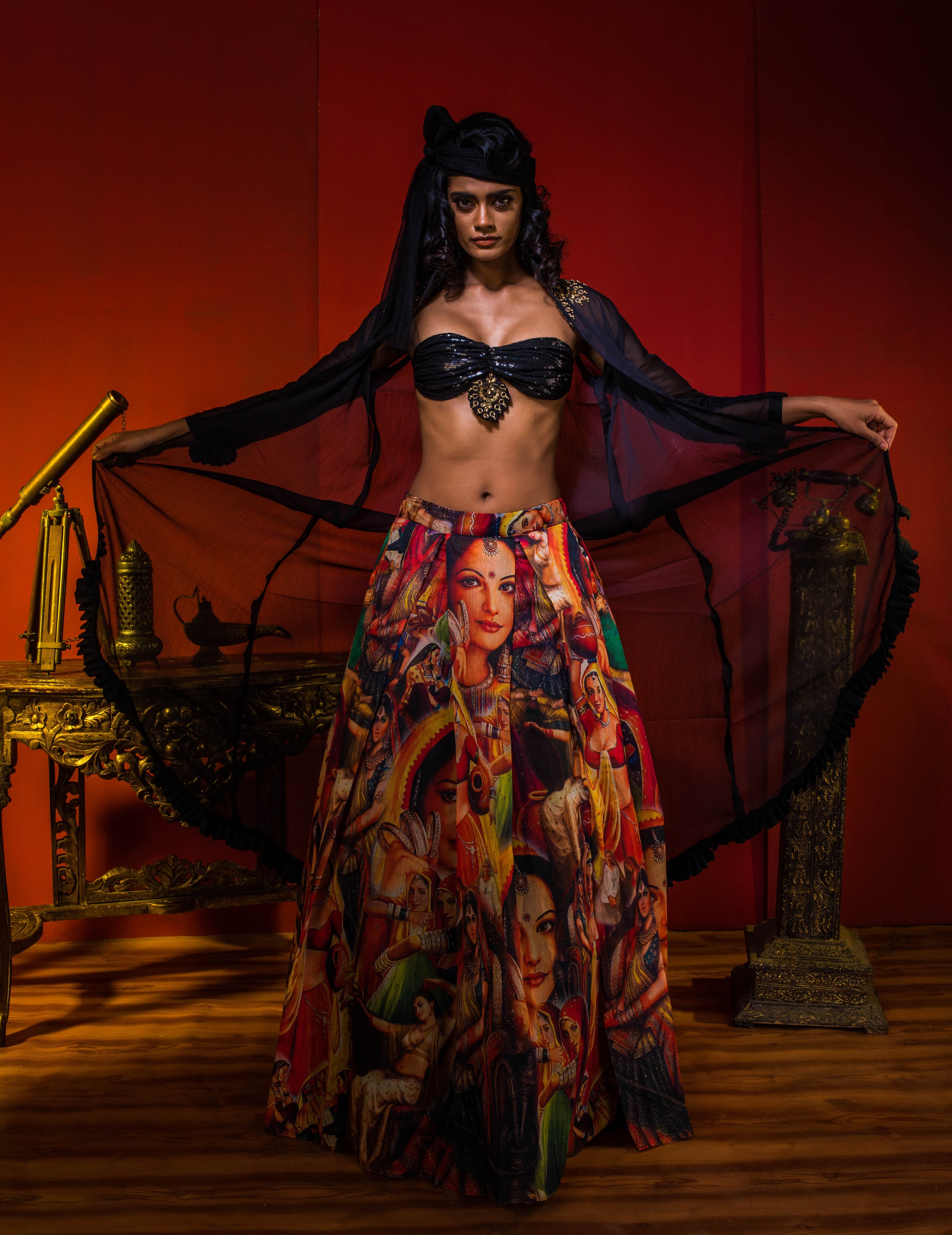 Supermodel Archana Akil Kumar in a heavily embellished black georgette bralette and long shrug paired with a printed colorful skirt revealing the bralette and the wide shrug in an antique setting.