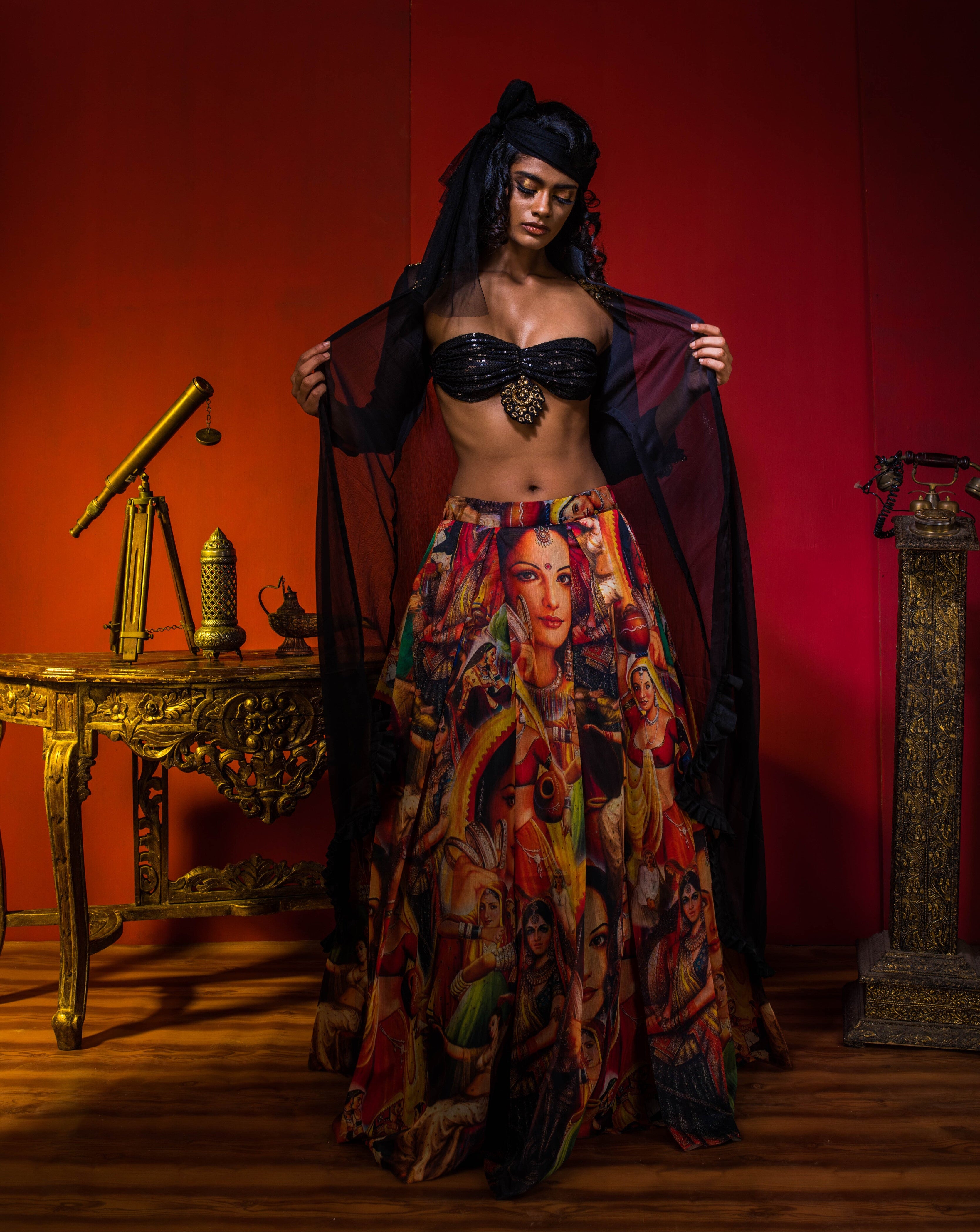 Supermodel Archana Akil Kumar in a heavily embellished black georgette bralette and long shrug paired with a printed colorful skirt revealing the bralette in an antique setting.