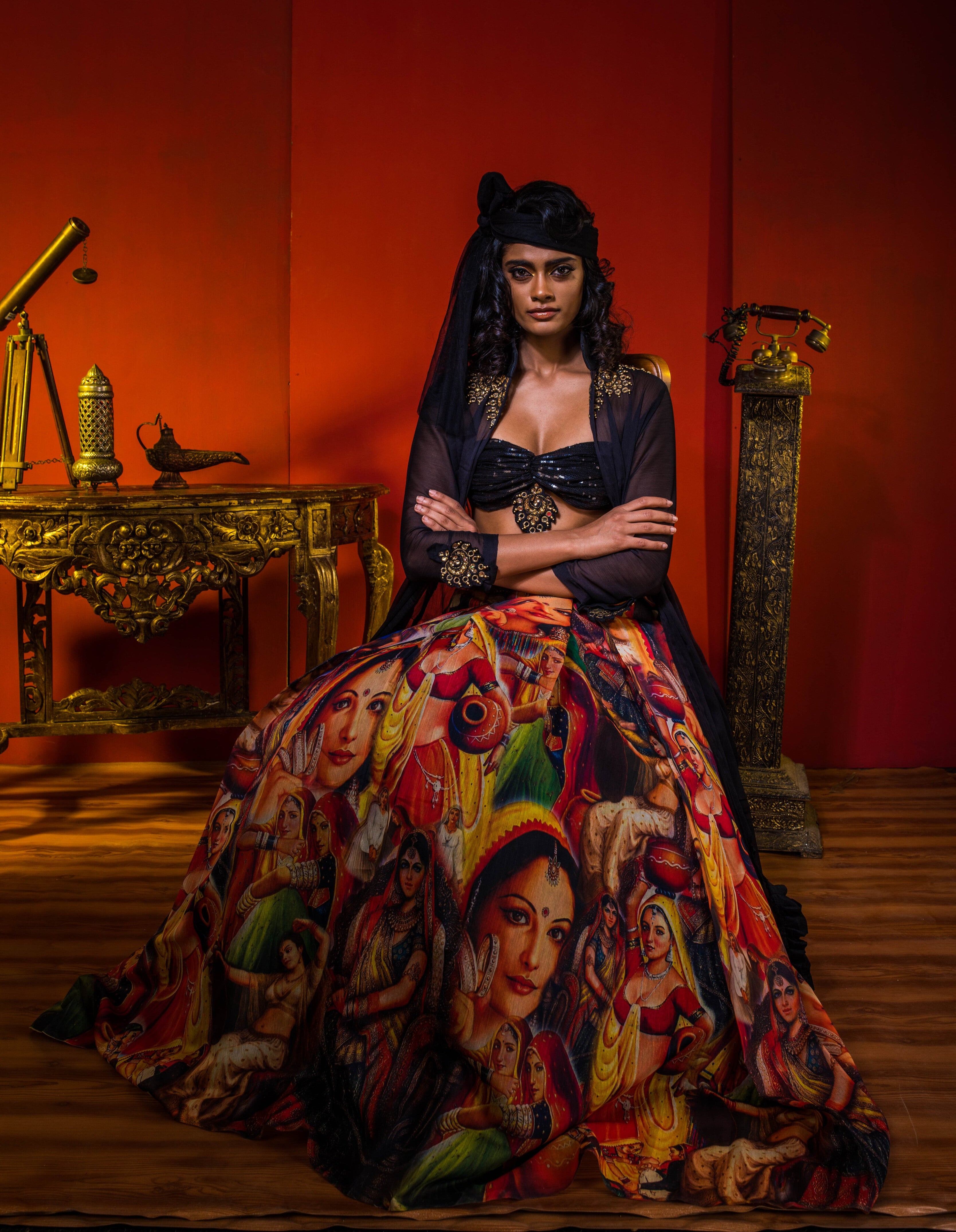 Supermodel Archana Akil Kumar in a heavily embellished black georgette bralette and long shrug paired with a printed colorful skirt sitting in an antique setting.