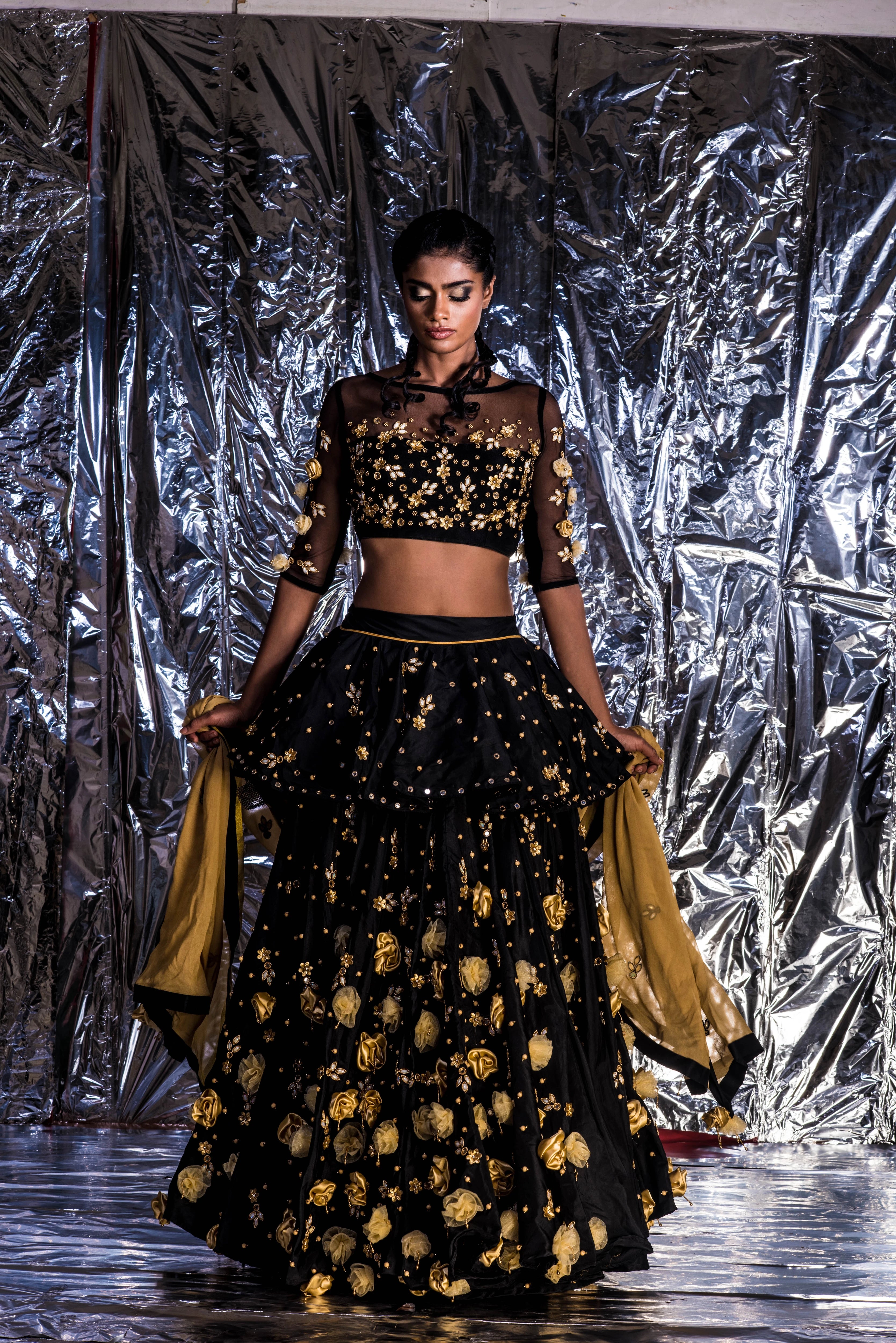 Supermodel Archana Akil Kumar looking down in a black taffeta lehenga with a gold georgette dupatta intricately handcrafted with appliques, pearls, mirror and beads.