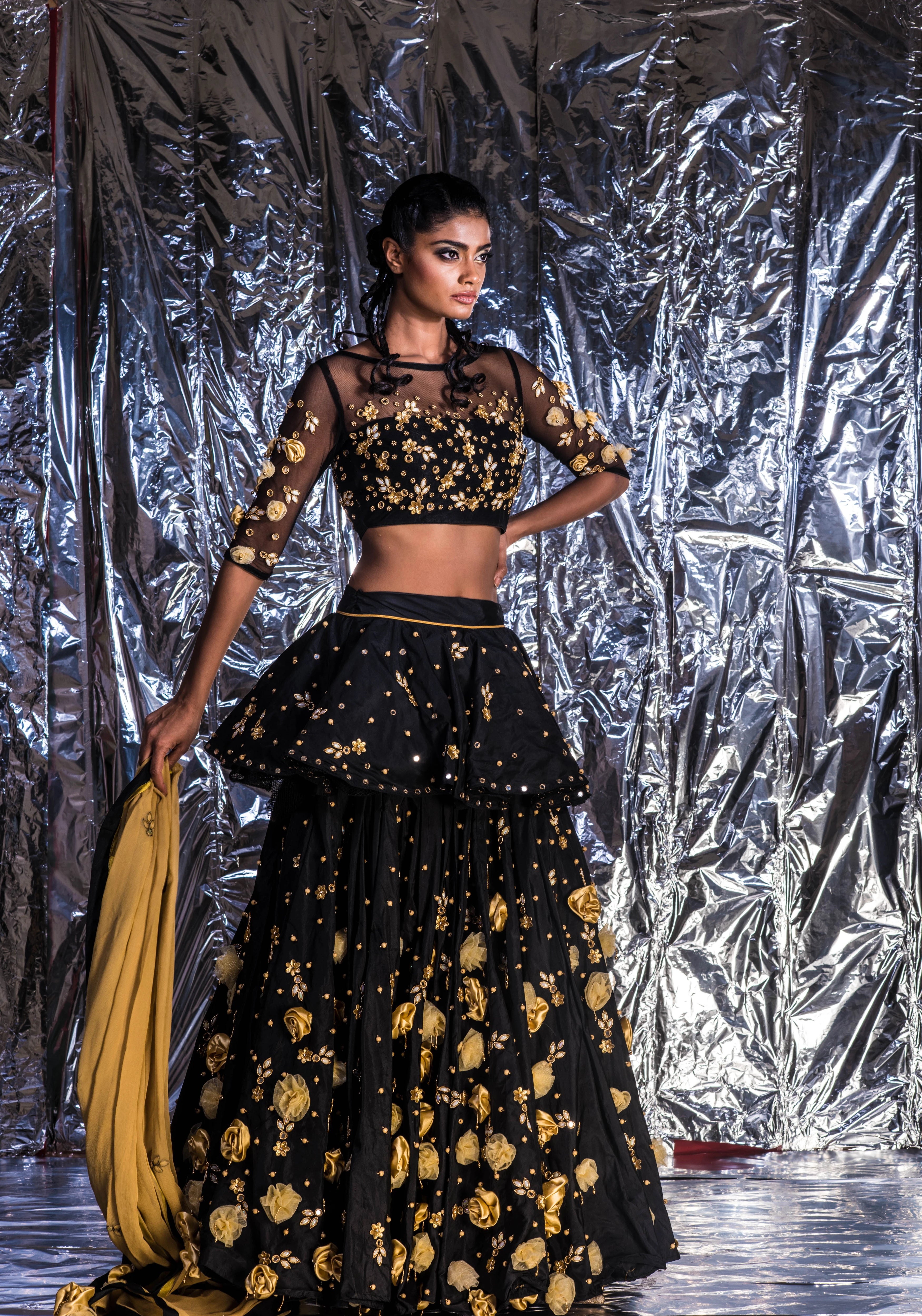 Supermodel Archana Akil Kumar posing by holding dupatta in a black taffeta lehenga with a gold georgette dupatta intricately handcrafted with appliques, pearls, mirror and beads.