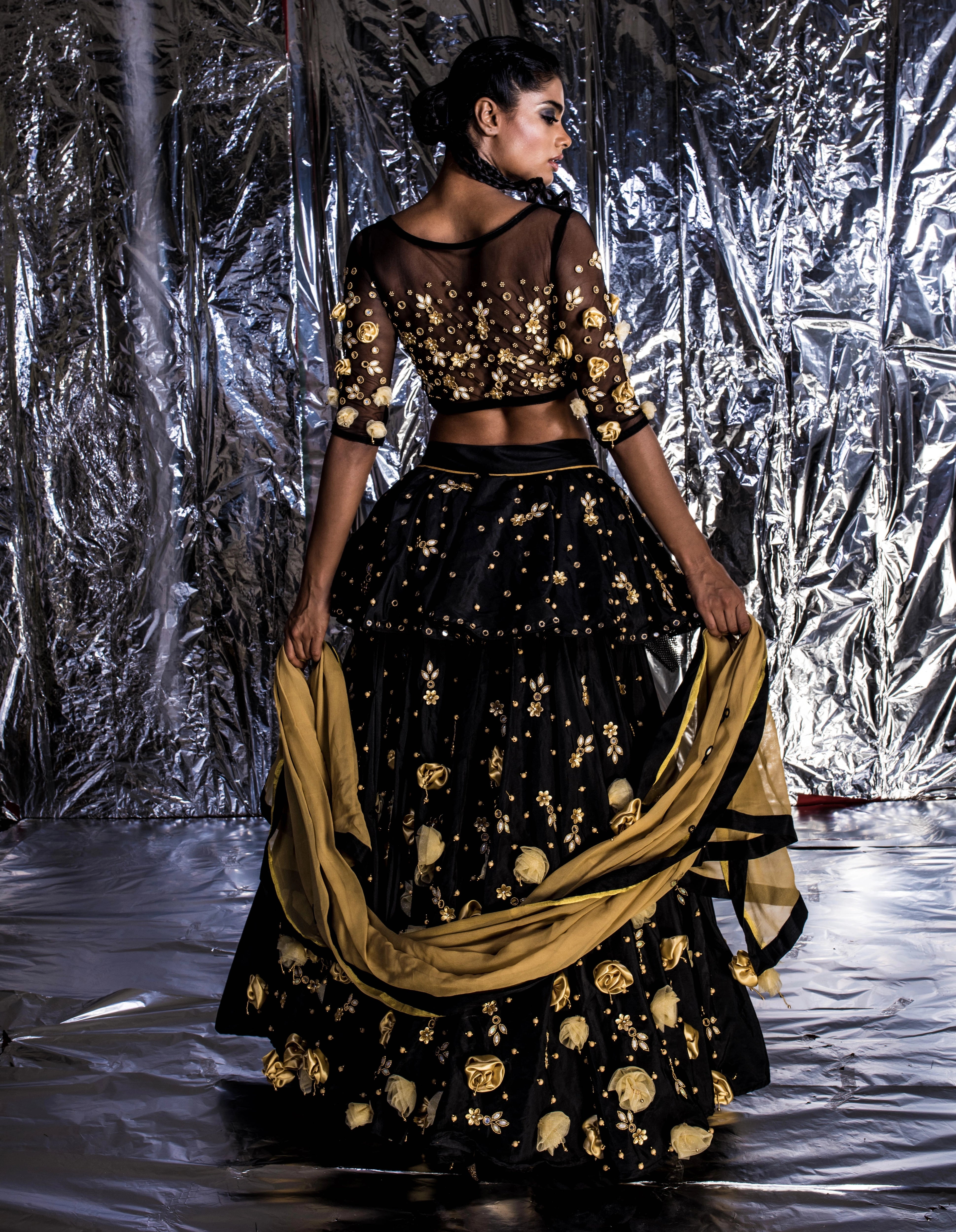 Supermodel Archana Akil Kumar posing for back design details in a black taffeta lehenga with a gold georgette dupatta intricately handcrafted with appliques, pearls, mirror and beads.