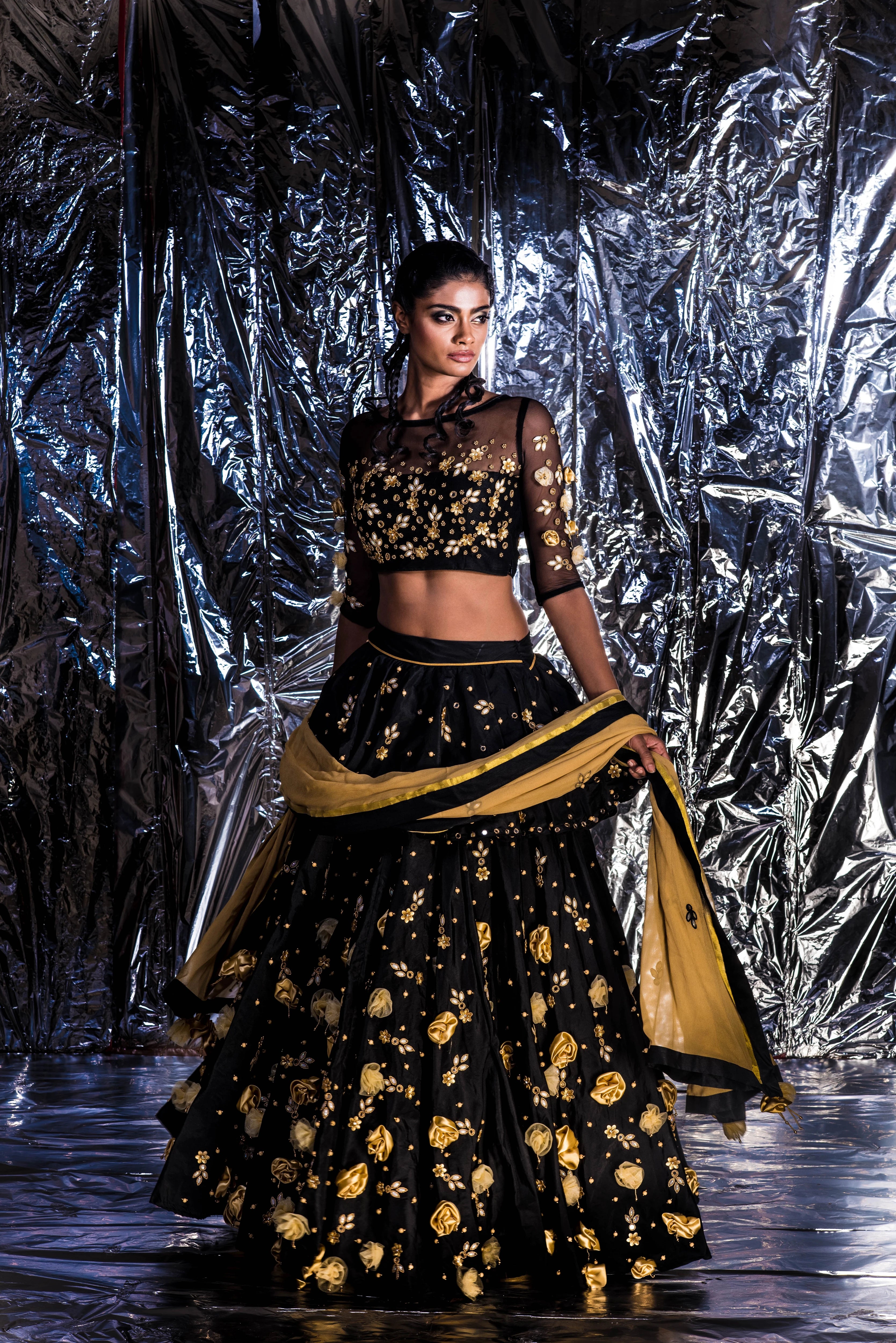 Supermodel Archana Akil Kumar posing in a black taffeta lehenga with a gold georgette dupatta intricately handcrafted with appliques, pearls, mirror and beads.
