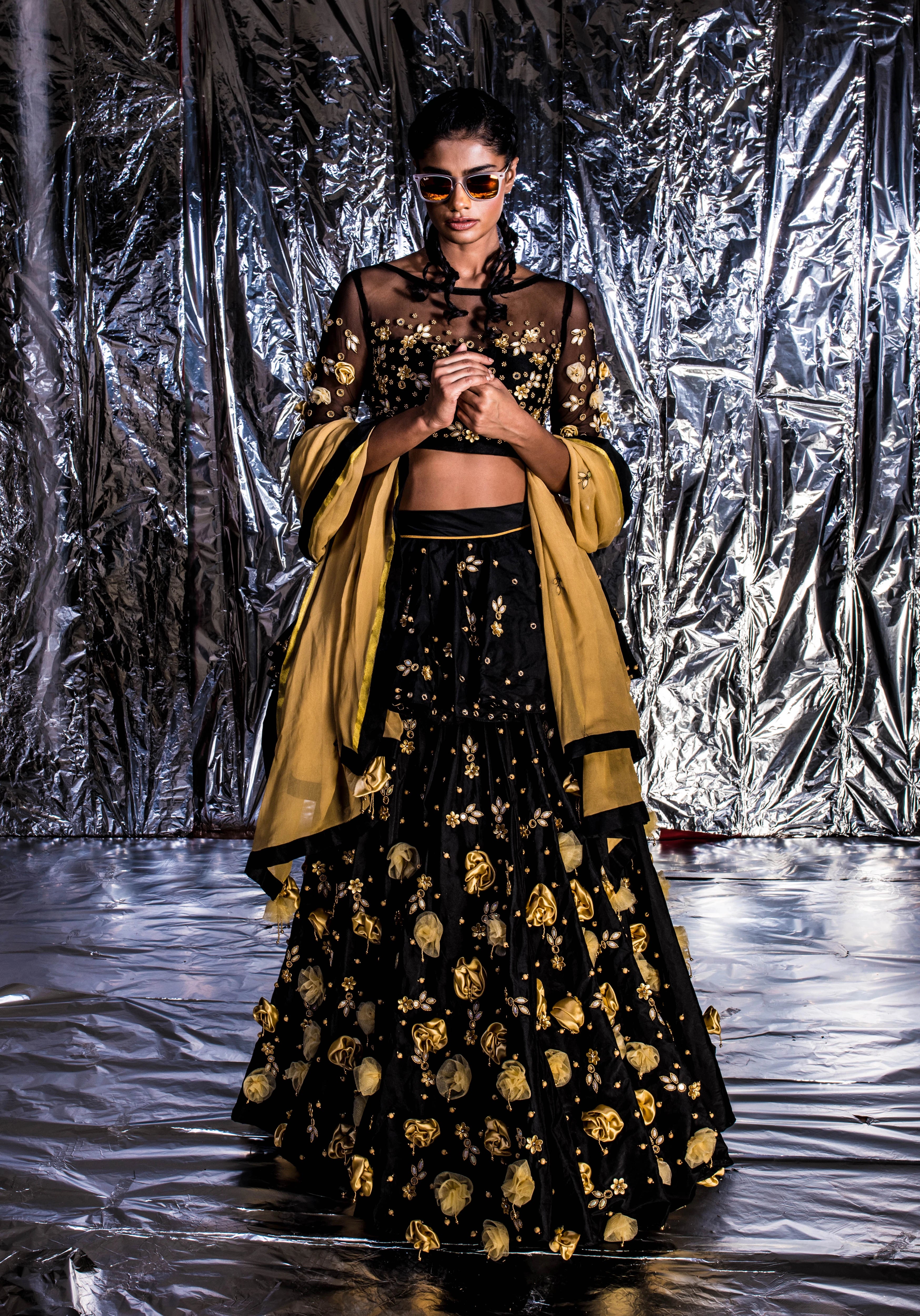 Supermodel Archana Akil Kumar posing in sunglasses in a black taffeta lehenga with a gold georgette dupatta intricately handcrafted with appliques, pearls, mirror and beads.