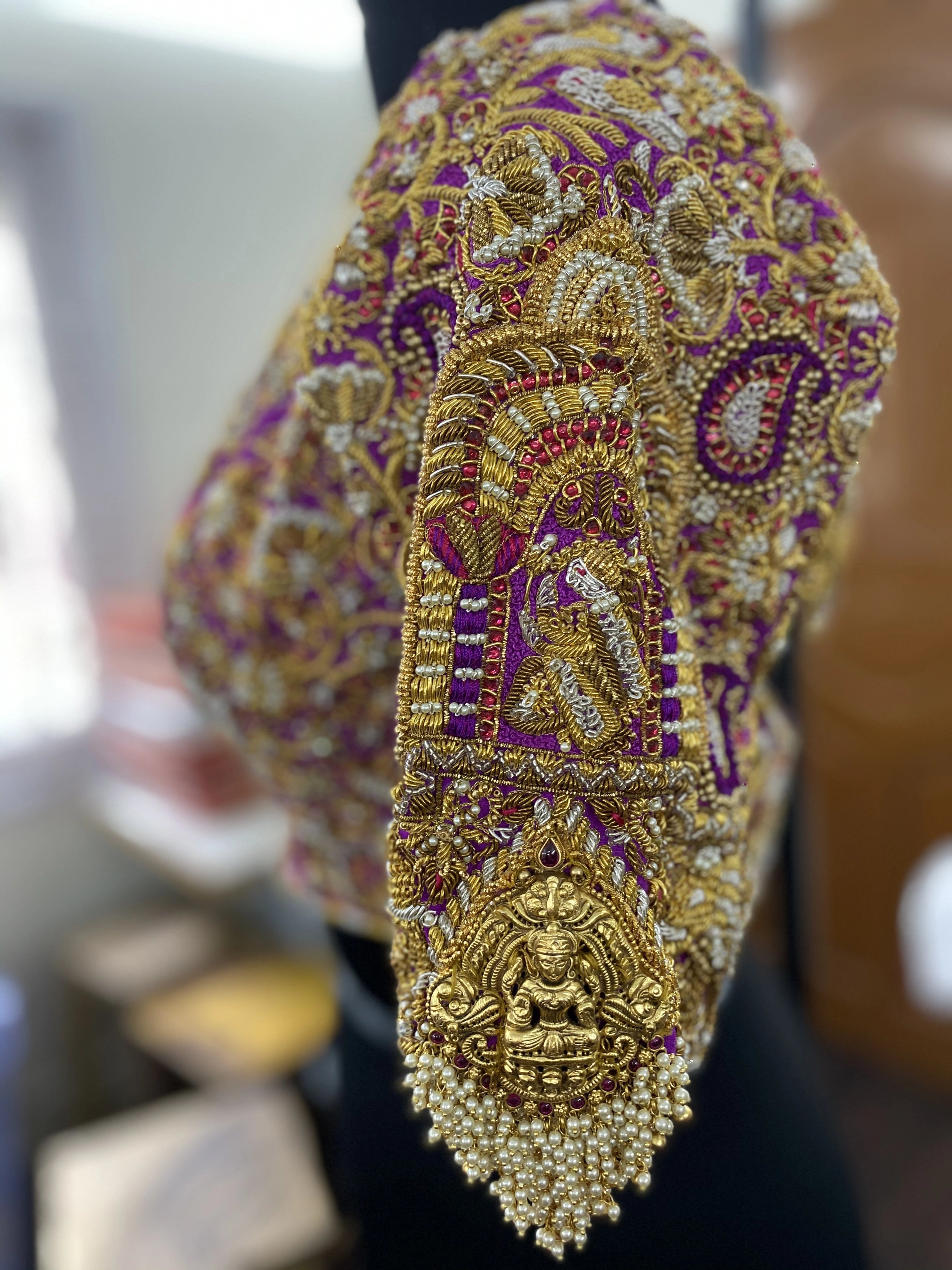 The sleeve detailings of a handcrafted palanquin concept magenta pink silk blouse with zardozi, kemp stones, pearls and resham knot work and goddess pendants on each sleeve. Designed by Archana Karthick