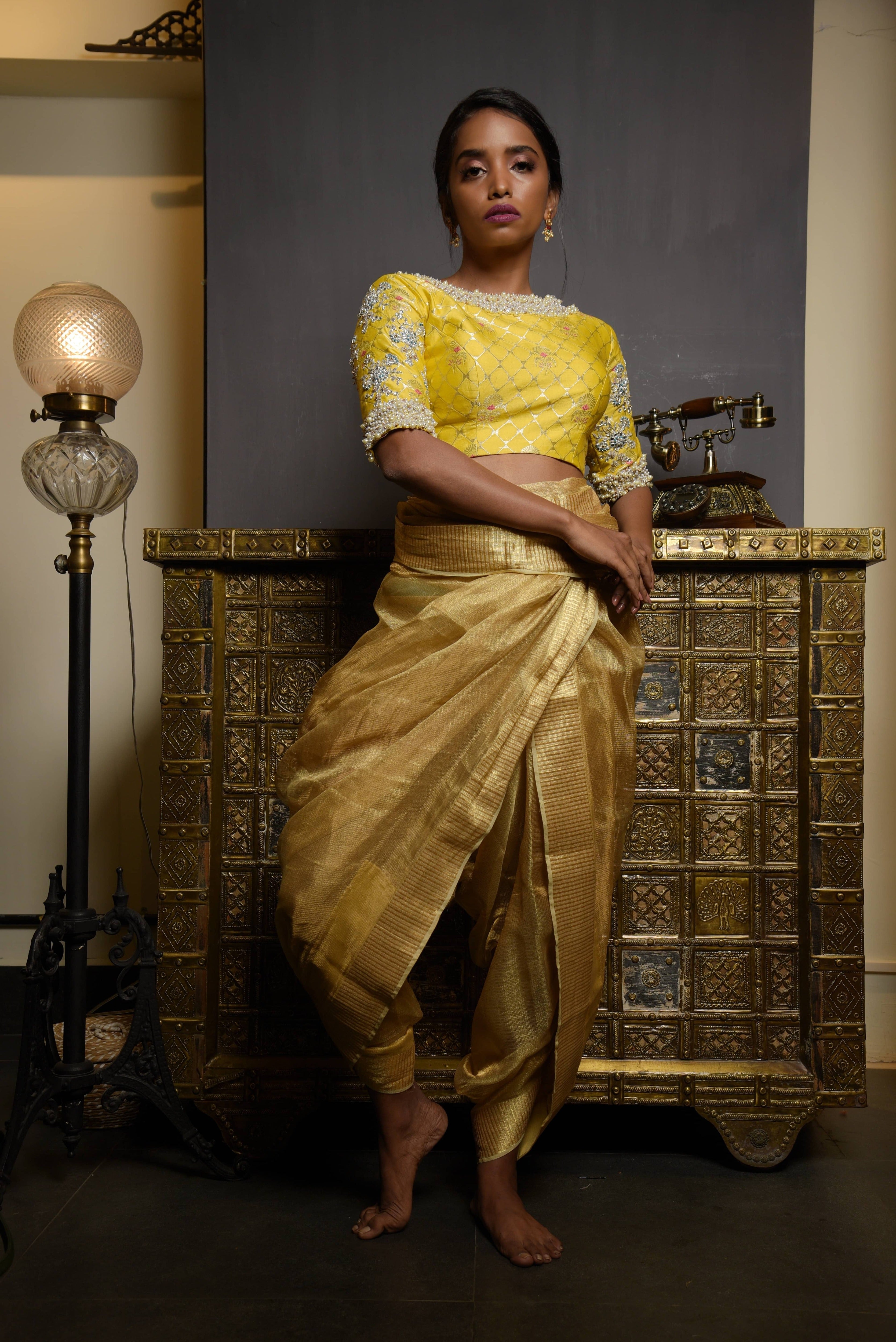 Model posing in a yellow banaras silk blouse with pearl embellishments on sleeves. The model has a dusky skin tone and has a tissue fabric draped for the bottom like a dhoti so that the attention is on the blouse.