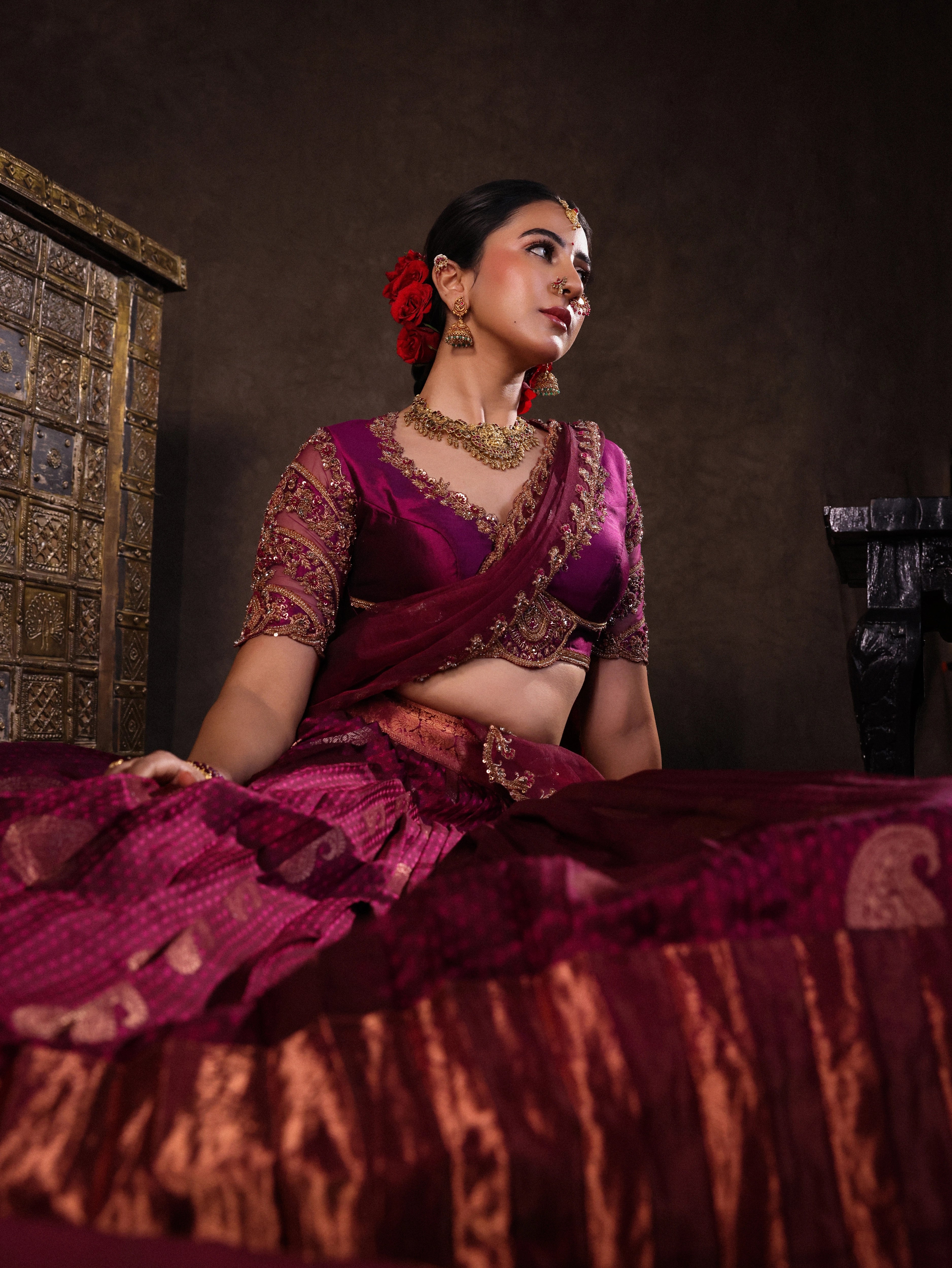 Actress Akshaya Hariharan seated in dark magenta kanjeevaram silk half saree with glass bangles and NAC jewellery.