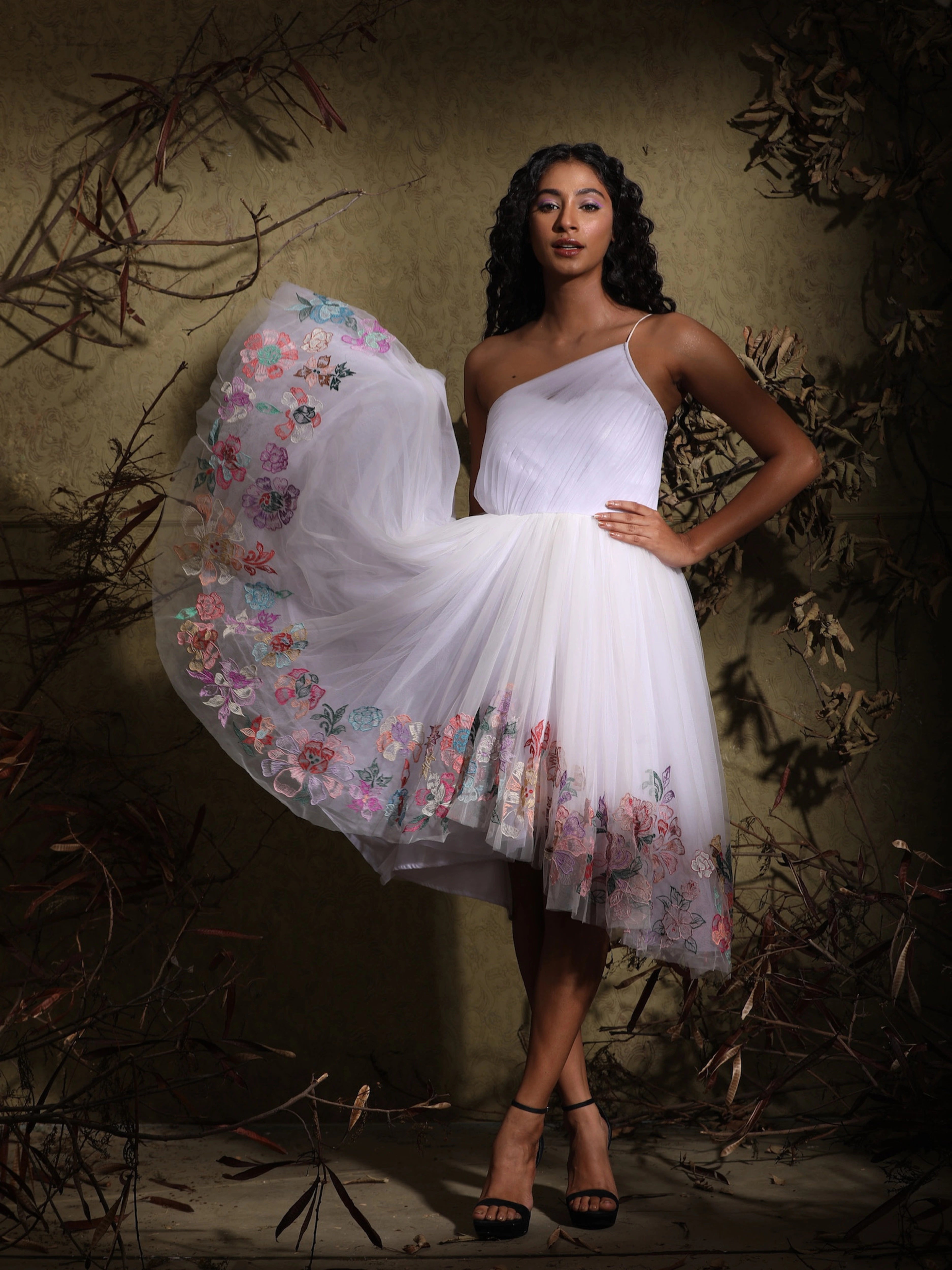 Anukreethy Vas, Miss India 2018, in a white one-shoulder tulle dress with vibrant pastel floral embroidery, twirling for a playful, elegant look by Archana Karthick. Perfect designer cocktail dress for women.