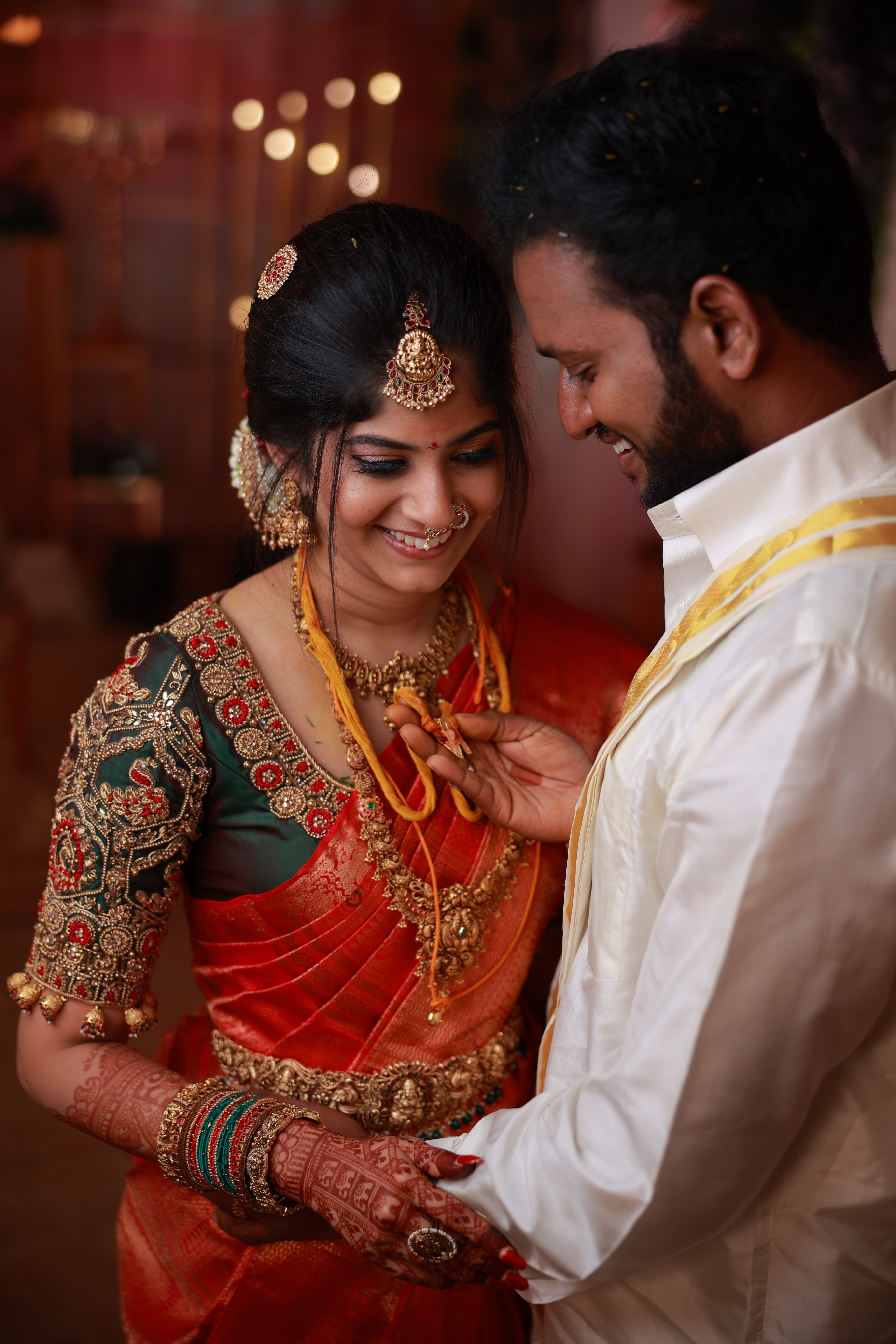 Kaviya, a bride is in a green silk blouse designed by Archana Karthick. She is looking down and smiling while the groom is lovingly holding her "Thaali", which is a symbol of their union, in his hand. The blouse has been handcrafted with intricate detailings involving beads, resham,zardozi and the blouse sleeves also have "jhumkas" at the seam.