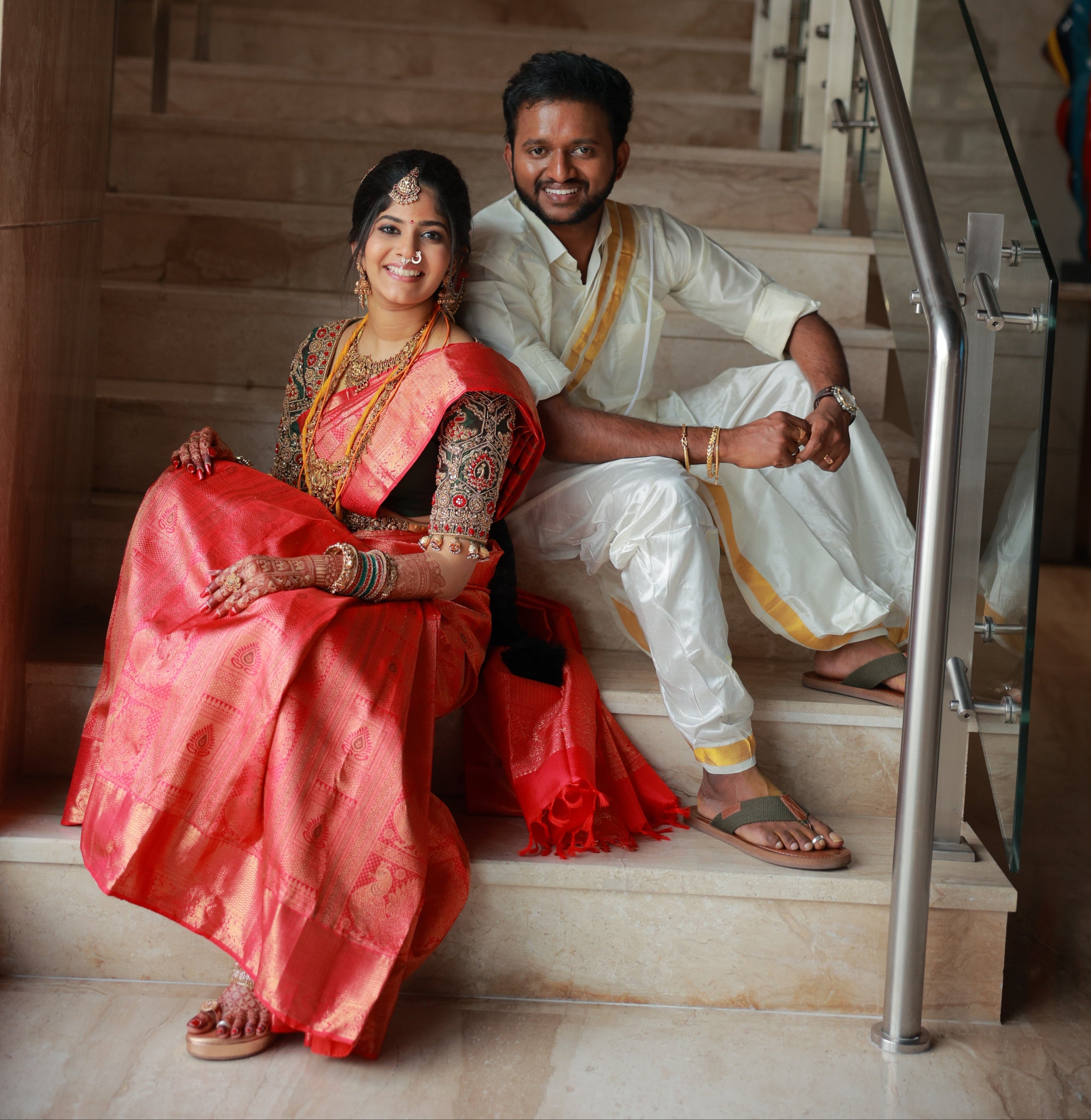 Kaviya, a bride is in a green silk blouse designed by Archana Karthick. She is posing for th epicture wiht the groom. They are both sitting on the stairs and looking at the camera. The blouse has been handcrafted with intricate detailings involving beads, resham,zardozi and the blouse sleeves also have "jhumkas" at the seam. The bride's mehendi is seen on her left hand.