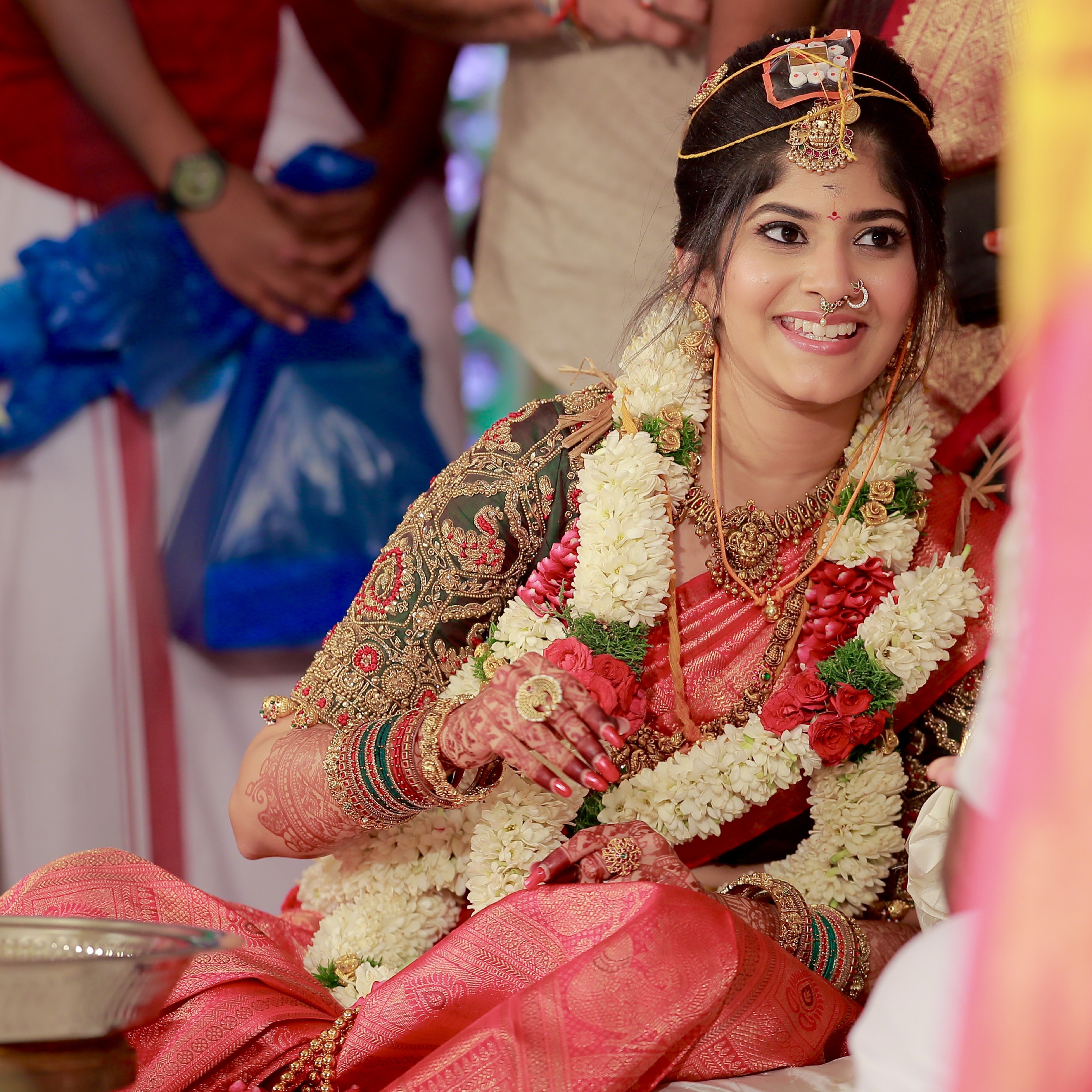 Kaviya, a bride is in a green silk blouse designed by Archana Karthick. She is smiling and looks lovely with the garland. The blouse has been handcrafted with intricate detailings involving beads, resham,zardozi and the blouse sleeves also have "jhumkas" at the seam.