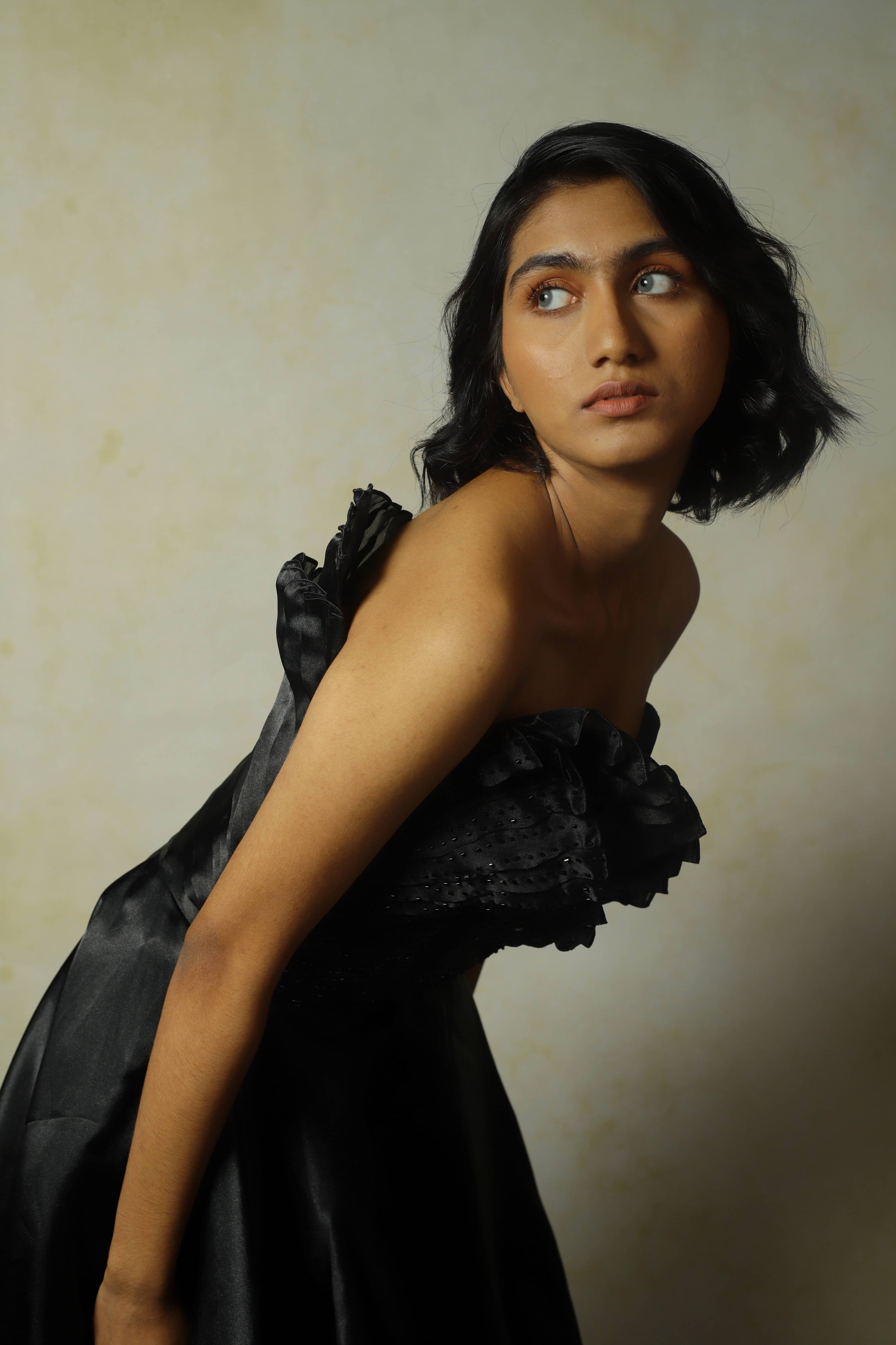 model posing in black tissue organza with structured upper body, bent forward and looking to her right. 