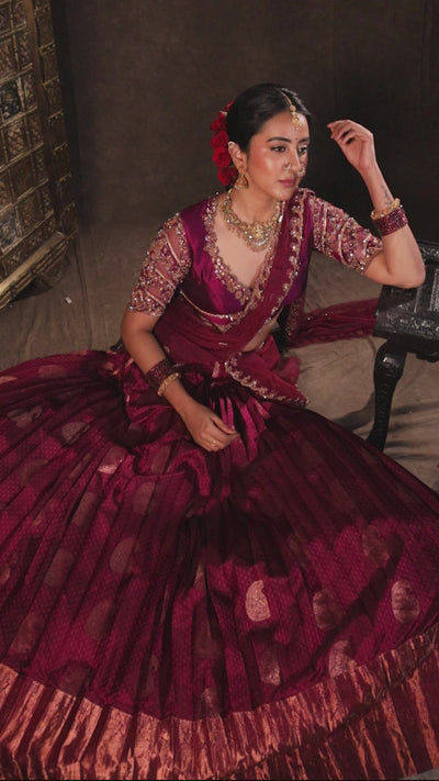 Actress Akshaya Hariharan in a campaign video in a dark magenta silk half saree set handcrafted with zardozi, resham, cutdana, sequins & rhinestones. Team Archana Karthick completed the style with dark magenta glass bangles, a ring, jhumkas, nose ring and a maang tikka.