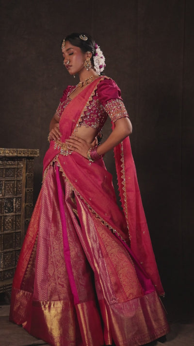 Model Gayathri Dhanasekar in a campaign video in a pink & orange silk half saree handcrafted with zardozi, cutdana (bugle beads), resham (silk thread), sequins and rhinestones. Team Archana Karthick completed the style with pink glass bangles, a ring, a choker, jhumkas, nose ring and a maang tikka.