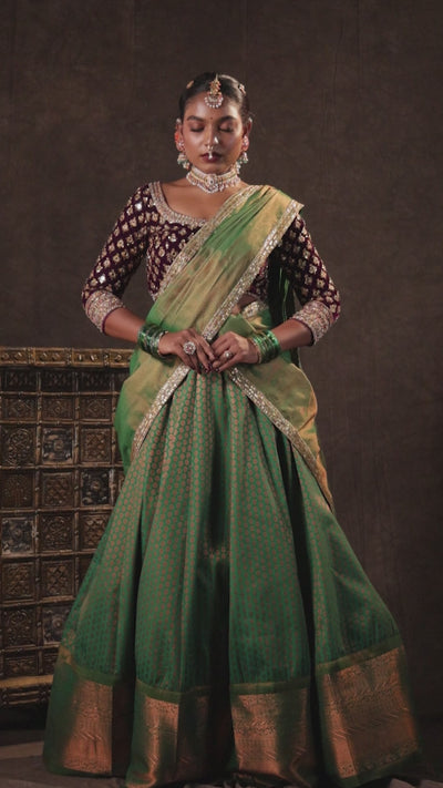Model Ashika Crystal for a campaign video in a green and purple half saree set with a velvet blouse, tissue silk dupatta and brocade skirt handcrafted with zardozi, mirror, zari, cutdana and sequins. Team Archana Karthick completed the style with green glass bangles, a ring, a choker, jhumkas, nose ring and a maang tikka.