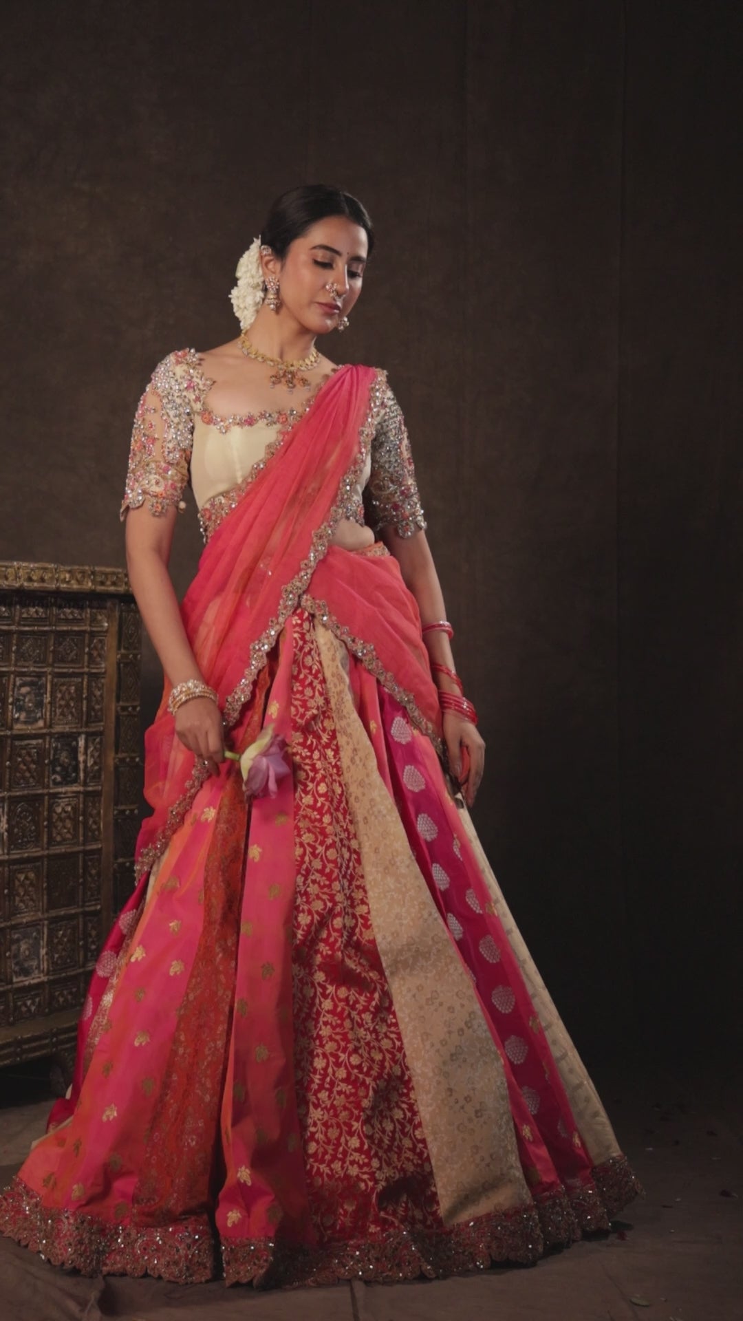 Actress Akshaya Hariharan in a campaign video in an ivory & pink brocade half saree set with tulle sleeves & dupatta. Team Archana Karthick completed the style with purple glass bangles, a ring, jhumkas, nose ring and a maang tikka.